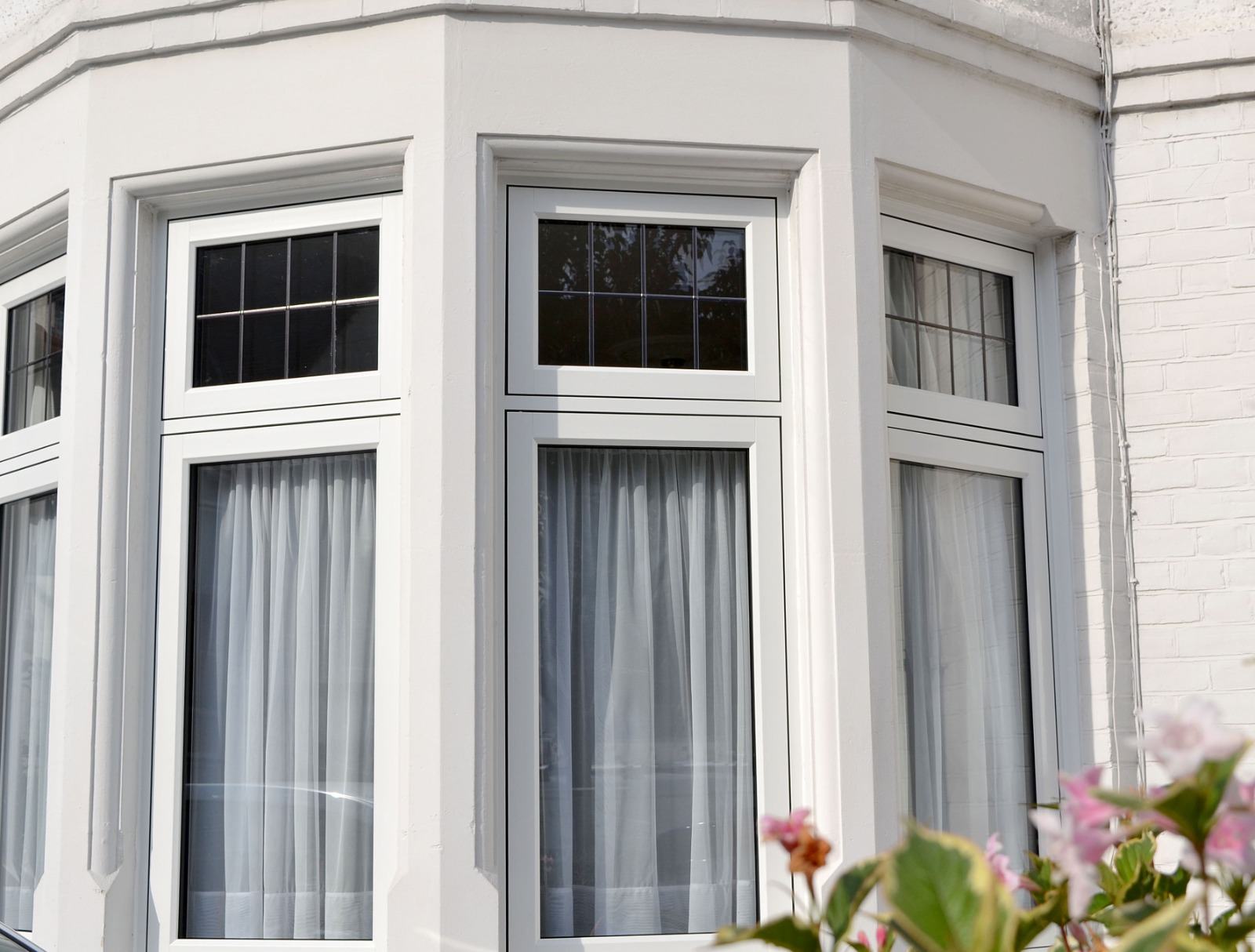 Close-up of a white uPVC bay window with slim top-opening vents in a painted render period bay