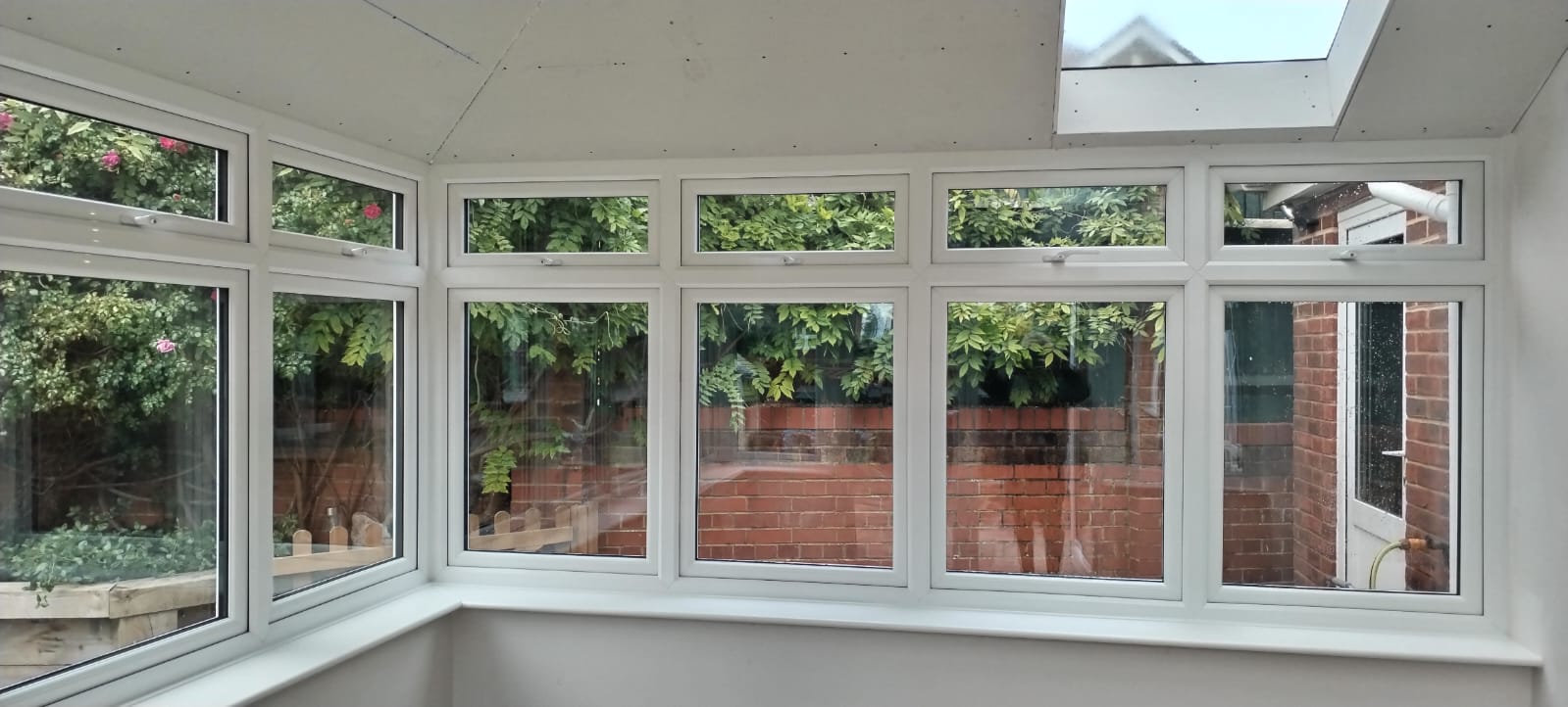 Bright conservatory interior with white uPVC casement windows, top-opening vents and a rooflight overlooking the garden