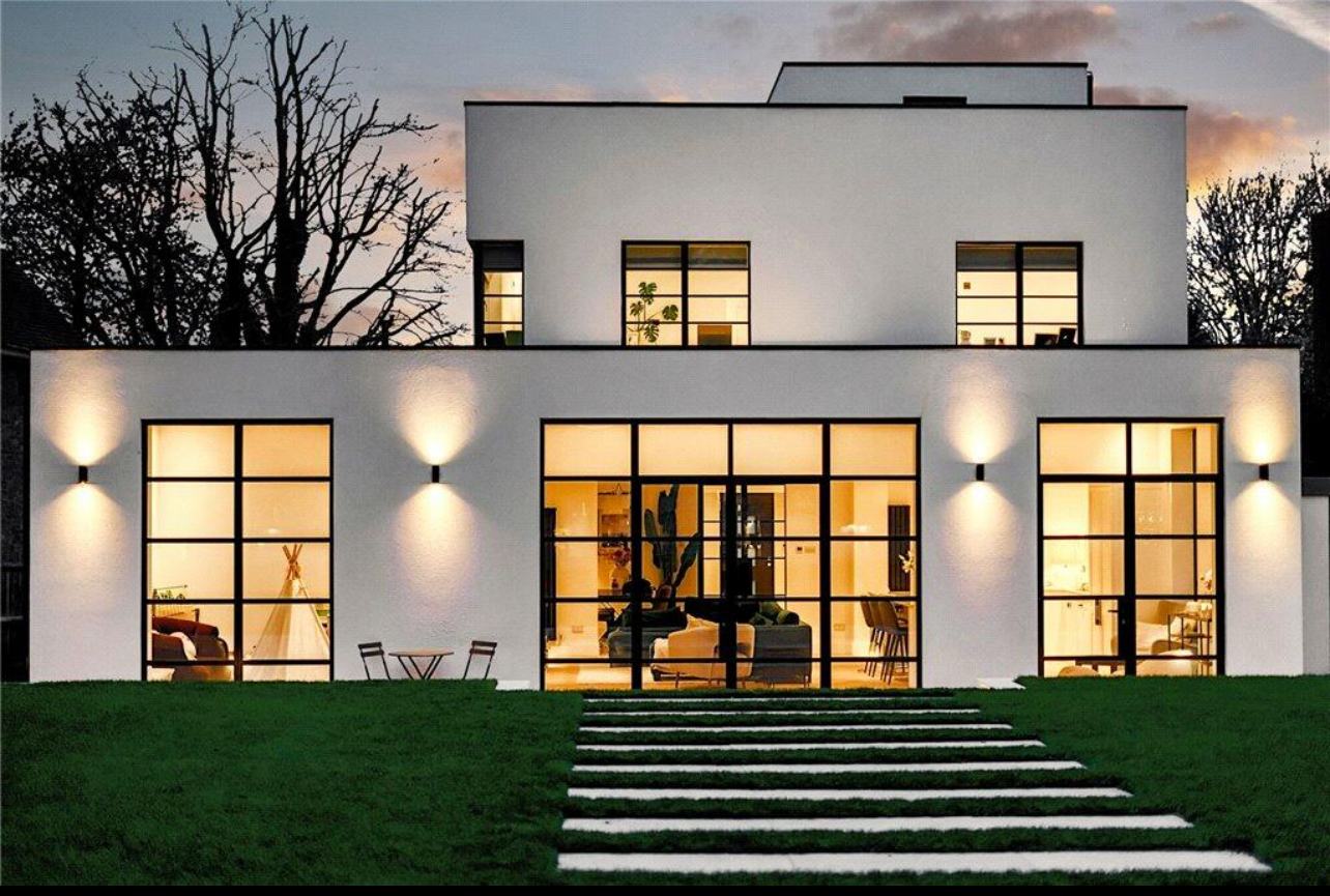 Modern white rendered home in Kent with black aluminium bi-fold doors and full-height Crittall-style windows at dusk