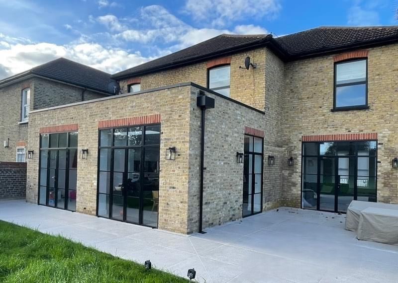 Rear yellow-brick extension fitted with black Crittall-style aluminium bi-fold doors and matching French doors on a London home