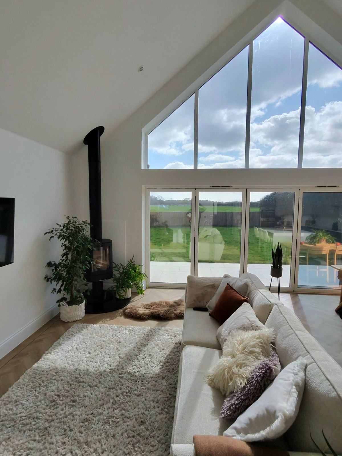 Vaulted lounge interior with full-height gable feature window and white bi-fold doors overlooking Kent countryside