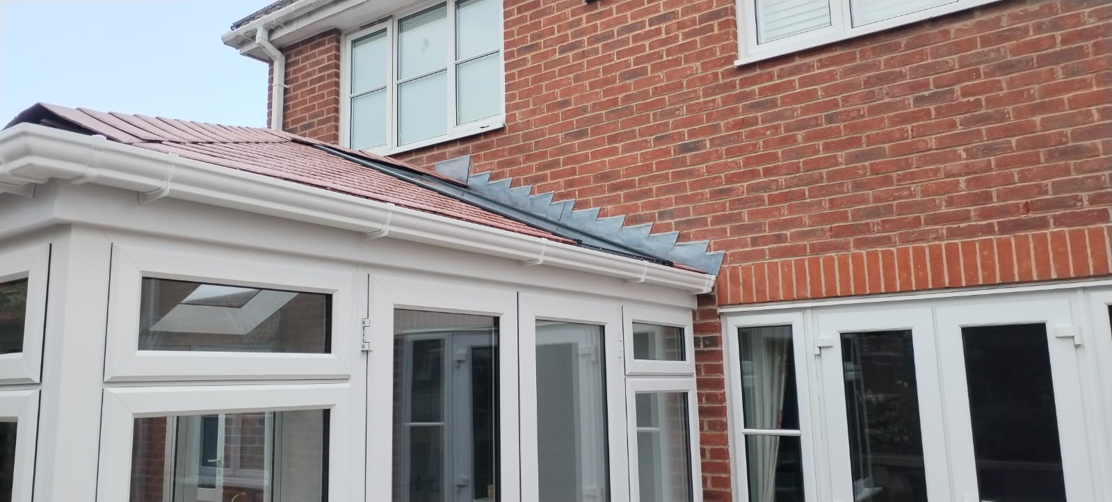 White uPVC conservatory exterior with new tiled roof and lead flashing joining a red-brick house