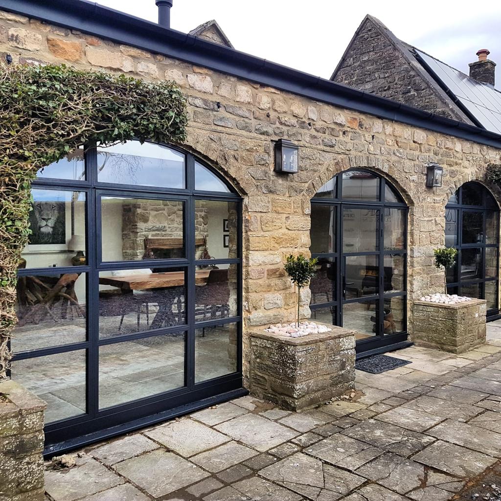 Stone barn conversion in Kent with arched aluminium patio doors and heritage window frames