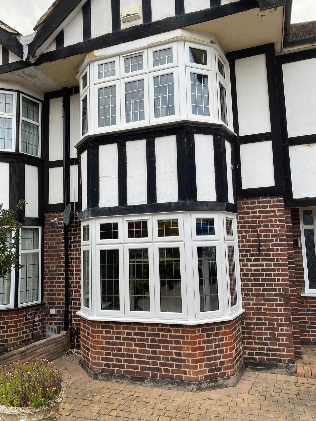 Two-storey white uPVC bay windows with leaded glazing fitted to a mock-Tudor semi-detached home