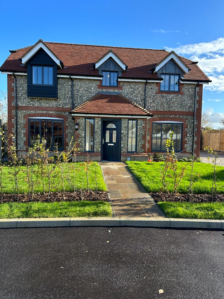 New-build flint and red-brick cottage with anthracite grey aluminium windows and a black composite front door installed by Swift Home Improvements