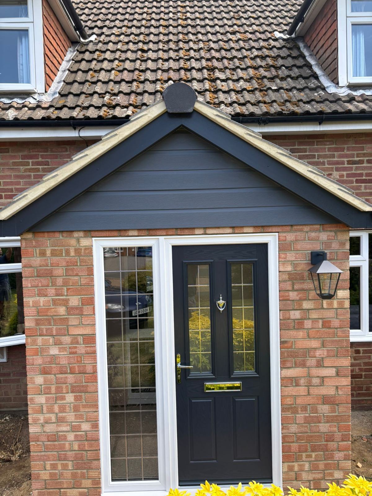 Anthracite grey composite front door with side glazed panel under a newly clad gable porch roofline on a brick home