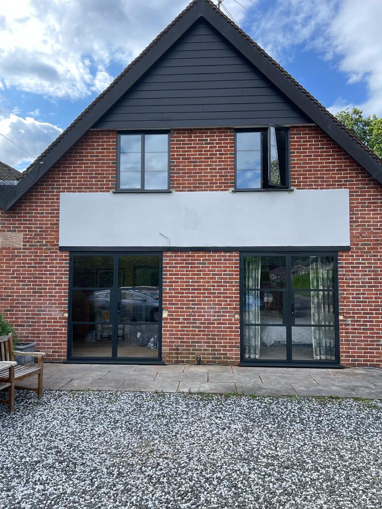 Pair of anthracite grey aluminium bi-fold doors installed on the rear of a red-brick Kent home with painted gable