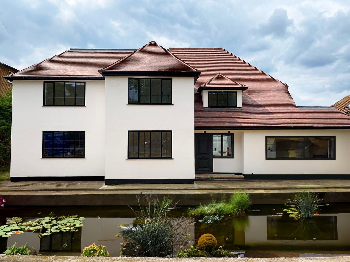 Large detached Kent home with new tall casement windows and dark aluminium frames overlooking a pond